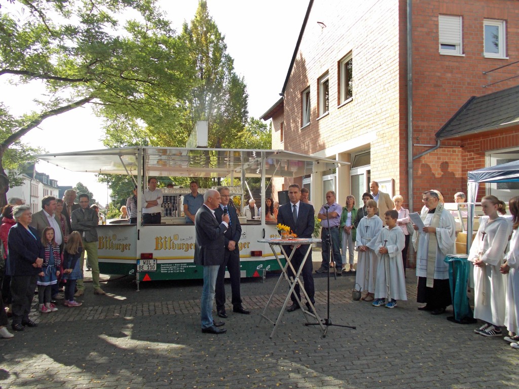 Das Bild zeigt Ortsvorsteher Peter van der Heyde (Bildmitte), Ludwig Thetard und Bürgermeister Joachim Rodenkirch sowie rechts Pfarrer Josef Karst mit seinen Messdienern, im Hintergrund rechts das Pfarrheim. Foto: Matthias Faas
