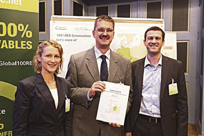 Roland Wernig bei der Siegelübergabe mit Yannick Régnier  (europ. Projektkoordination 100% RES Communities) und  Pia Buschmann (deENet, dt. Projektkkordination). Foto: © deENet