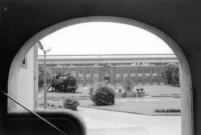 Blick vom Verwaltungsgebäude auf die Richthalle des Ausbesserungswerks Trier am 1. Juli 1977. Als Denkmal wurde 1974 die Lokomotive der Baureihe 86 aufgestellt. 1985 ist die Lokomotive wieder für Sonderfahrten aufbereitet und auf richtige Gleise gestellt worden. Aufnahme Martin Kreckler