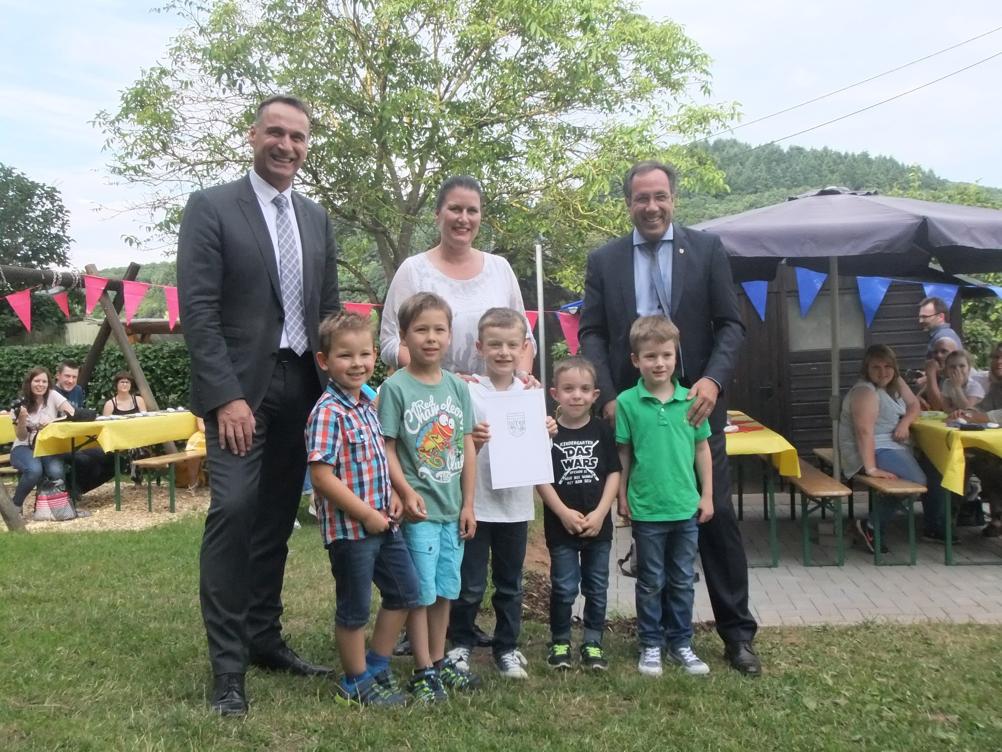 Bürgermeister Joachim Rodenkirch (links), Kindertagesstättenleiterin Yvonne Eckes-Brost und Landrat Gregor Eibes (rechts) freuen sich mit den Kindern über die Auszeichnung – Foto: privat