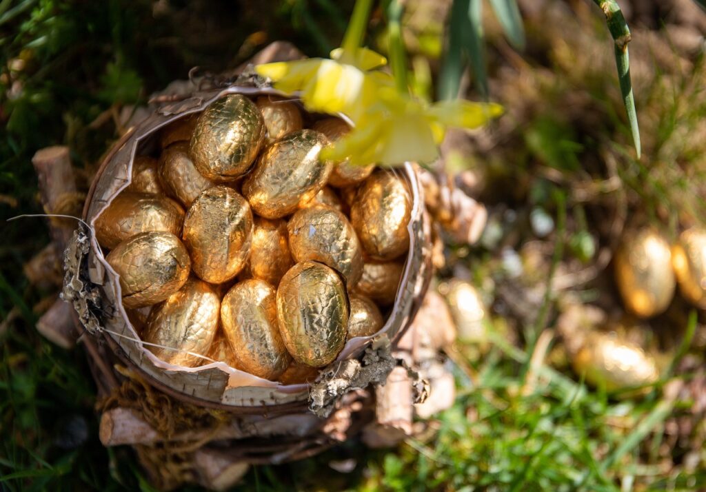 Ein Korb gefüllt mit goldenen Schokoeiern steht im Wald.