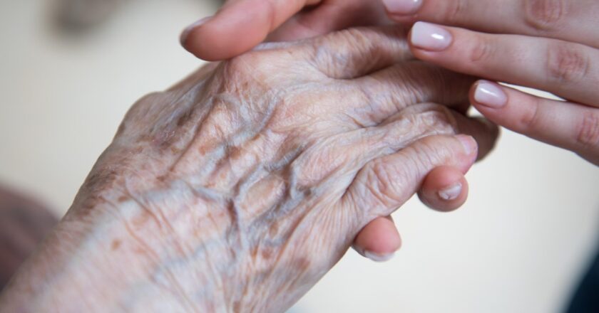 Eine Pflegerin hält die Hand einer Seniorin in einem Pflegeheim.
