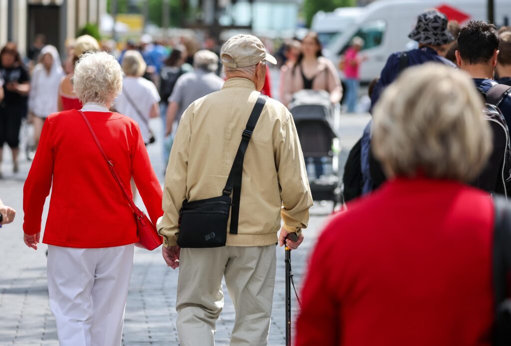 Senioren gehen Hand in Hand durch eine befüllte Innenstadt.