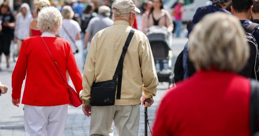 Senioren gehen Hand in Hand durch eine befüllte Innenstadt.