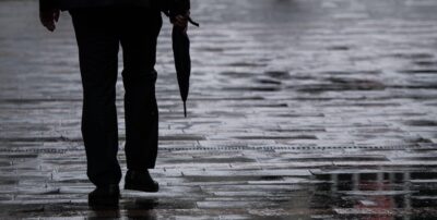 Ein Mann geht mit einem Regenschirm in der Hand durch eine Fußgängerzone.