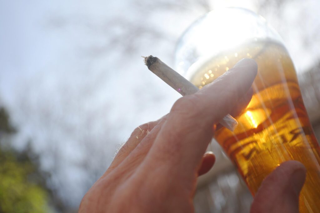 Eine Zigarette in der Hand und ein Bier in Nahaufnahme vor einem blauen Himmel.