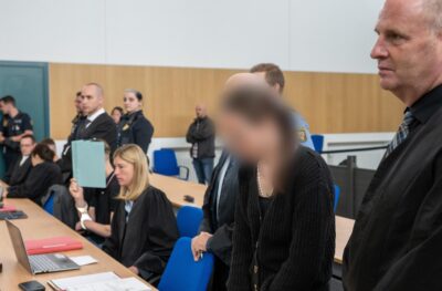 Mehrere Menschen stehen während eines Gerichtsprozesses im Gerichtssaal.