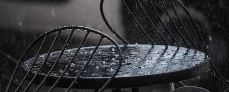 Regen prasselt auf einen Tisch eines Cafés im Außenbereich.