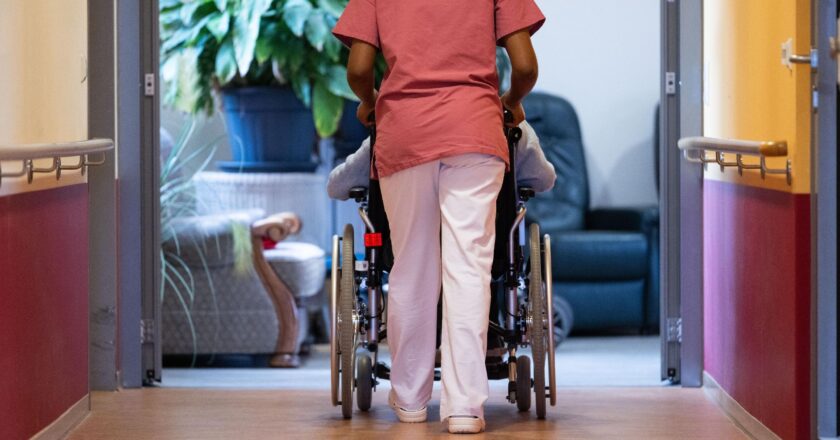 Eine Bewohnerin eines Pflegeheims wird von einer Pflegerin einen Gang entlangeschoben.
