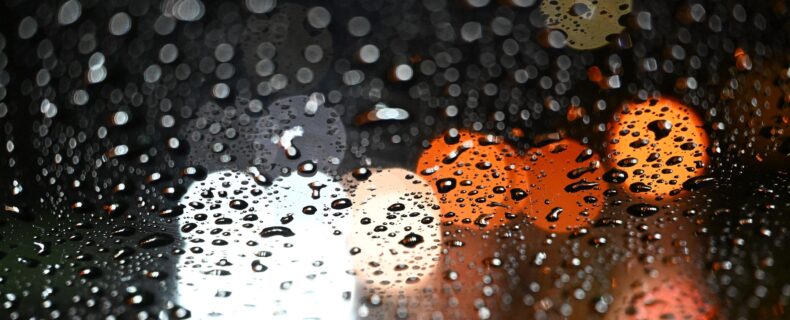 Lichter von Autos scheinen durch eine Scheibe, die mit Regentropfen bedeckt ist.