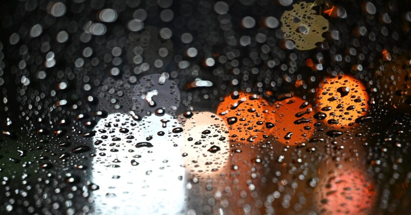 Lichter von Autos scheinen durch eine Scheibe, die mit Regentropfen bedeckt ist.