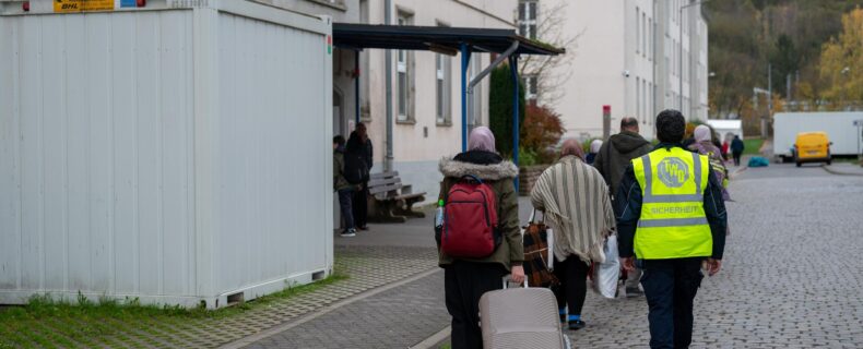 Neuangekommene Flüchtlinge gehen mit einem Koffer in eine Aufnahmeeinrichtung.