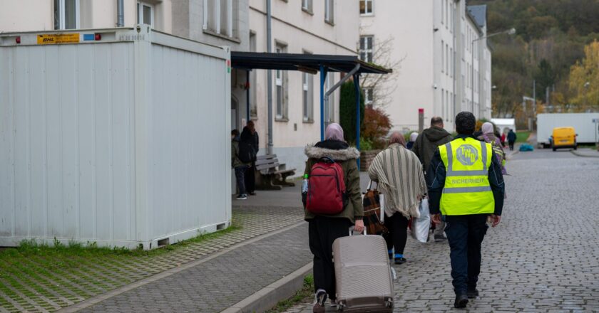 Neuangekommene Flüchtlinge gehen mit einem Koffer in eine Aufnahmeeinrichtung.